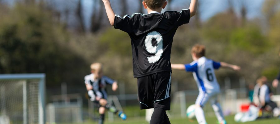 Young boys playing soccer on green soccer pitch. Trademarks have been removed.